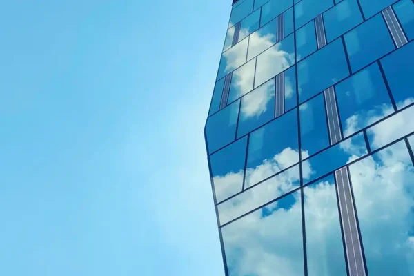 Close-up glass facade of office building with reflection of blue sky.